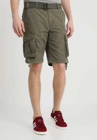 Pantaloni cargo in cotone verde oliva, con molteplici tasche laterali, una cintura e una vestibilità casual. Abbinati a sneakers in suede rosse.