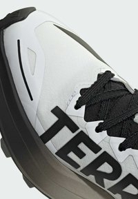 Baskets en textile blanc avec accents noirs, arborant un grand logo "TERRE", une surface texturée et une semelle extérieure noire épaisse. Les lacets sont noirs.