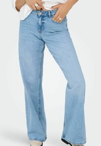 Lyseblå vide jeans laget av denim, med høy midje, forkrommede lommer foran og subtile voldtegn nær hoftene.