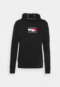 Black hoodie with front pocket and drawstring hood, featuring a Tommy Hilfiger logo patch with a handshake design in red, white, and navy blue.
