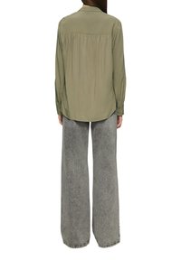 Olijfgroene overhemd met knopen en een geplooide achterkant, gecombineerd met losse, lichtgrijze wijde jeans. Gladde stof, casual ontwerp en lange mouwen.