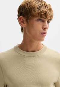 Beige, tekstuuriinilla neulottu poolopaita, jossa on pyöreä pääntie. Ominaisuuksiin kuuluu tiheä kudontakuvio ja ribbineck. Silkkinen, pehmeä kangas.