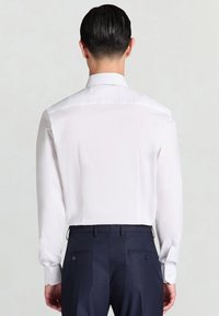 Weißes Langarmhemd mit glatter Textur, klassischem Kragen und tailliertem Rücken. Kombiniert mit marineblauen, strukturierten Hosen.
