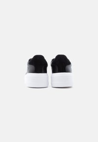 Ζευγάρι μαύρα sneakers με πυκνές λευκές σόλες, εμφανιζόμενα από πίσω, με την ένδειξη "LOVEMOSCHINO" χαραγμένη στις φτέρνες.