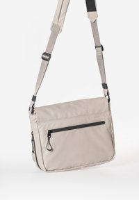 Borsa a tracolla beige realizzata in materiale resistente, dotata di una tracolla regolabile, di una tasca con zip frontale e di una texture liscia.