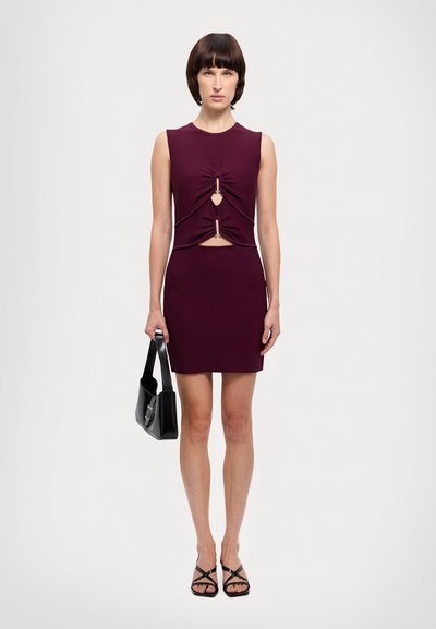 Sleevless dress yang cocok di badan berwarna burgundy tua dengan potongan dan detail twist di pinggang. Dipadukan dengan tas tangan hitam dan sandal tali.