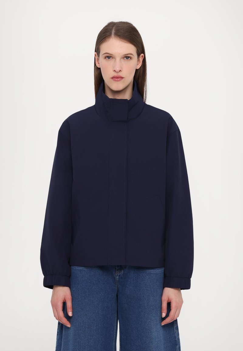 Navy blue bomber jacket with a high collar, dropped shoulders, and elastic cuffs. Features side pockets and a smooth, matte texture.