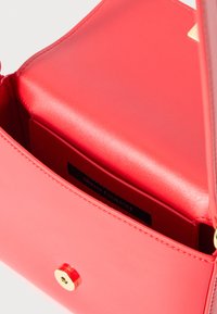 Κόκκινη δερμάτινη τσάντα χεριού με λεία υφή, χρυσές λεπτομέρειες και κλείσιμο με κουμπί. Το εσωτερικό διαθέτει ετικέτα Armani Exchange και θήκη για κάρτες.