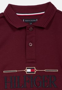 Polo shirt bordeaux avec un col côtelé, une patte de boutonnage à deux boutons et un logo "HILFIGER" brodé avec un design de pagaie.