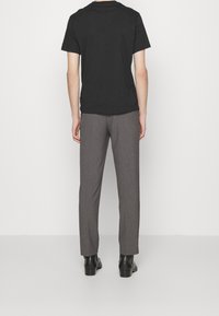 Zwart katoenen T-shirt gecombineerd met grijze op maat gemaakte broek. De broek heeft een subtiele textuur en een rechte pijp. Afgewerkt met zwarte schoenen.