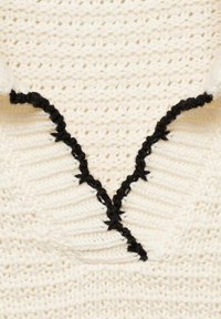 Creme strikket sweater med V-udskæring, prydet med sort zigzag-kant langs halsudskæringen og strukturerede ribdetaljer.