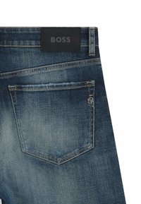 Jeans in denim blu medio con una leggera sfumatura. Presentano un'etichetta in pelle nera sulla cintura e un accento metallico sulla tasca posteriore.