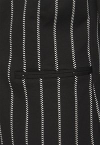 Svart tyg med vertikala vita ränder. Har en horisontell ficka med svart kant. Materialet verkar slätt med en lätt stretch.