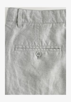 Pelēki džinsi ar gludu tekstūru, aizmugures kabata ar pogu un jostas cilpas ap jostasvietu.