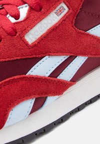 Κοντινό πλάνο κόκκινου αθλητικο ύ παπουτσιού Reebok με λεπτομέρειες από σουέτ, ανοιχτά μπλε δερμάτινες ρίγες και το λογότυπο της Union Jack στο πλάι.