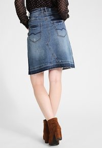 Tummansininen denimhame, jossa on repaleinen helma, takataskut ja vartalonmyötäinen muotoilu. Yhdistettynä ruskeisiin mokkanahkasaappaisiin.