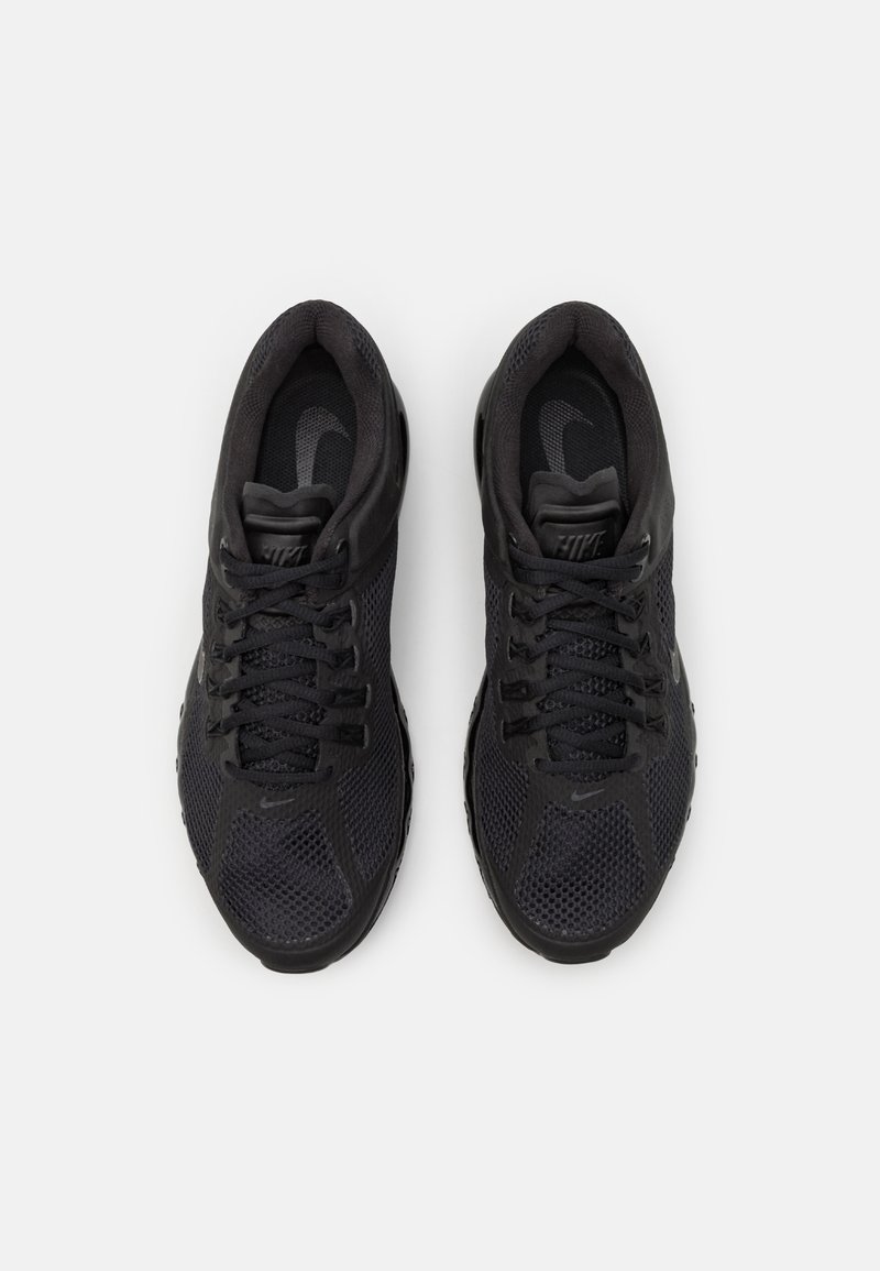 Zapatos deportivos negros con parte superior de malla, punta redondeada y cordones. Presentan un logo sutil y una suela texturizada para mayor tracción.