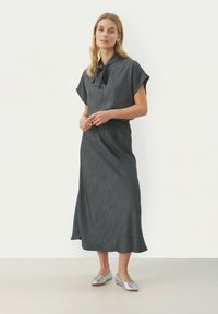 Donkergrijze midi-jurk met een kraag en korte mouwen. Heeft een verzamelde taille en een subtiele textuurstof. Zilveren flat shoes.