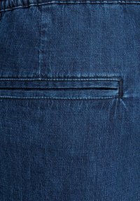 Sötétkék farmeranyag, melyen egy lapos záródású hátsó zseb található, sima textúrával és diszkrét varrási részletekkel.
