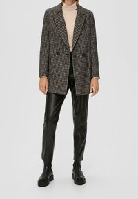 Schwarzer und weißer Hahnentrittmuster-Blazer mit einem doppelt-knöpfbaren Design, kombiniert mit schwarzen Lederhosen und Stiefeletten. Glatte Stoffstruktur.