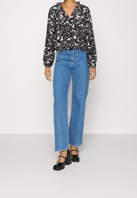 Blusa floreale in bianco e nero con maniche a palloncino, abbinata a jeans a gamba dritta a vita alta di un blu chiaro e scarpe con plateau nere.