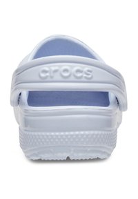 Des Crocs blancs avec un bout fermé et une sangle arrière ajustable, présentant une adhérence texturée sur la semelle et une finition lisse et brillante.