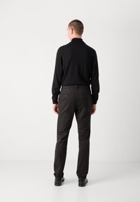 Zwarte lange mouwen trui gecombineerd met donkere broeken, met een rechte pasvorm en twee achterzakken. Glad, gestructureerd stof. Zwarte schoenen.
