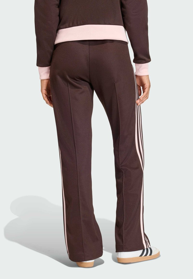 Brown athletic pants with pink accents, featuring a straight cut and side stripes. The material is smooth with a slight sheen.