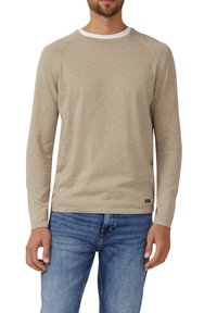 Beiges Langarmshirt mit Rundhalsausschnitt aus weichem Material, mit Raglanärmeln und weißem Kragenakzent. Getragen zu blauen Jeans.