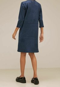 Marinblå klänning med trekvartslånga ärmar, textil med struktur, knälång fåll och en cirkulär knappstängning på baksidan. Svarta platåskor.