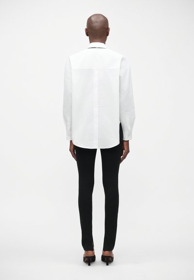 Witte lange mouwen blouse met knoopsluiting, gecombineerd met zwarte slim-fit broek met gespleten zomen en hoge hakken.