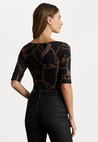 Top negru cu un model de lanț și panglică, cu un decolteu rotund și mâneci lungi până la cot, asortat cu blugi închiși la culoare cu talie înaltă.