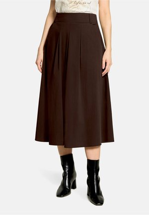 Woman wearing a dark brown midi skirt with front pleats and black heeled ankle boots, paired with a light top.