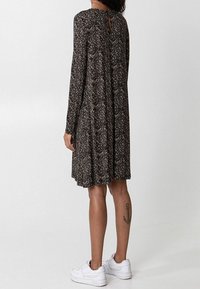 Robe noire à manches longues avec un motif floral, dos en trou de serrure, longueur au genou, accompagnée de baskets blanches.