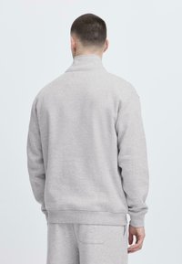 Grå hettegenser laget av myk stoff med høy krage, ribbestrikkede mansjetter og midjebånd, med en avslappet passform og uten synlige trykk.