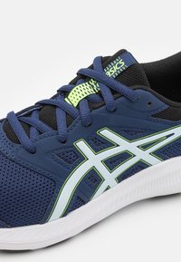 Chaussure de sport bleue en matériaux en maille et synthétiques, avec des accents blancs et vert fluo, une surface texturée et un design à lacets.