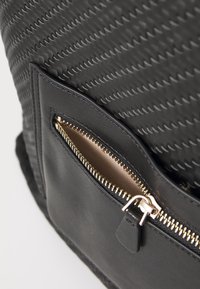 Schwarze Tasche mit gewebter Textur und einer glatten Ledertasche. Enthält einen goldenen Reißverschluss und einen kleinen Lederriegel-Akzent.