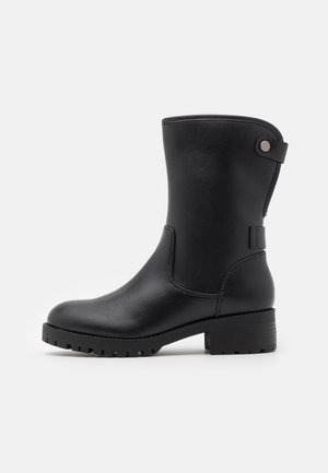 Botte en cuir noir jusqu'au milieu du mollet, avec semelle crantée, talon bloc et une bride avec un bouton rond en métal au sommet à l'arrière.
