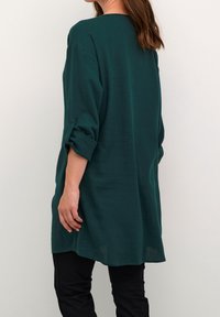 Teal langærmet skjorte med rullede manchetter, lavet af et letvægtsstof. Har en afslappet pasform og en afrundet kant bagpå.