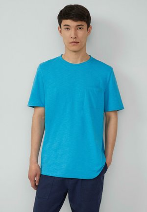 Short-sleeve blue t-shirt made of lightweight fabric, features a round neck and a chest pocket, paired with dark pants.