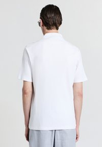 Polo shirt bianco a maniche corte con texture a coste e colletto standard, caratterizzato da orlo dritto e vestibilità rilassata. Design minimalista.