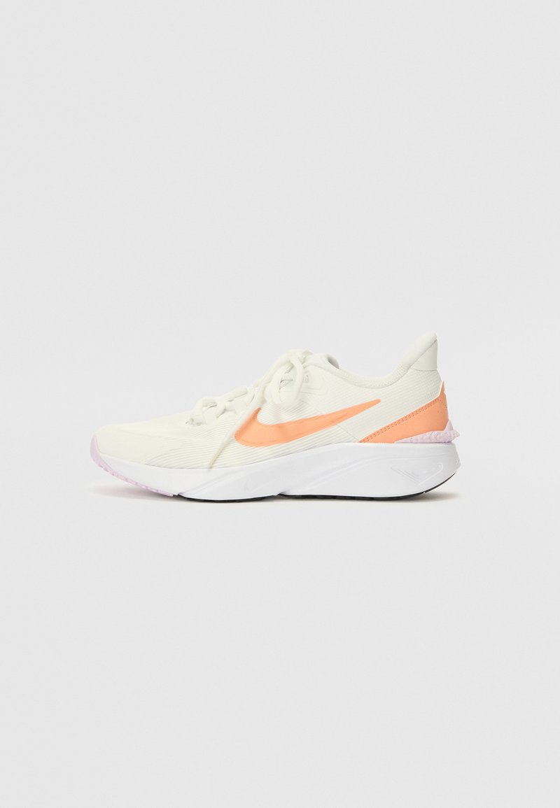 Zapatilla deportiva blanca con tela texturizada, detalles en naranja y punta redondeada. Cuenta con cordones y una suela acolchada con una sección rosa.