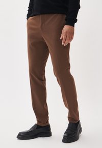 Bruna tapered byxor i mjukt tyg med en slät yta och sidofickor, kombinerade med svarta loafers.