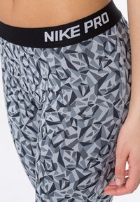 Legíny Nike Pro s geometrickým vzorem v odstínech šedi a černé, s černým pasem, na kterém je tučně napsáno „NIKE PRO“ bílými písmeny.