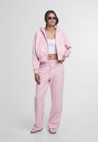 Set asortat de culoare roz deschis, format dintr-un hanorac scurt cu fermoar frontal și buzunare mari, complementar cu pantaloni de trening cu croială lejeră și talie elastică.