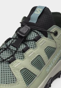 Lähikuva vihreästä Salomon-vaelluskenkästä, jossa on verkkomateriaalia, synteettisiä päällysteitä ja nopea kiristysnauhojen järjestelmä mustalla kielekkeellä.