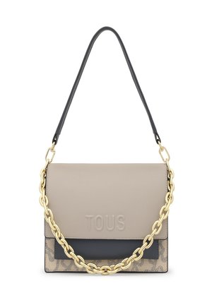 Bolso rectangular beige y negro con el logo "TOUS" en relieve, detalle de cadena dorada y asa de hombro negra sobre un fondo blanco.