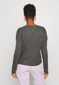 Maglione grigio a coste con maniche lunghe, scollatura rotonda e vestibilità rilassata. Indossato con pantaloni cargo di un leggero colore viola, che mettono in evidenza la lunghezza delle maniche e la texture.
