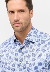 Camicia a manica corta con bottoni caratterizzata da una base azzurro chiaro con motivi botanici blu scuri, colletto classico e una texture del tessuto liscia.