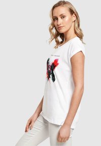 Weißes T-Shirt mit hochgekrempelten Ärmeln, das einen farbenfrohen Grafikdruck in Rot und Schwarz zeigt, aus weichem Baumwollmaterial gefertigt.